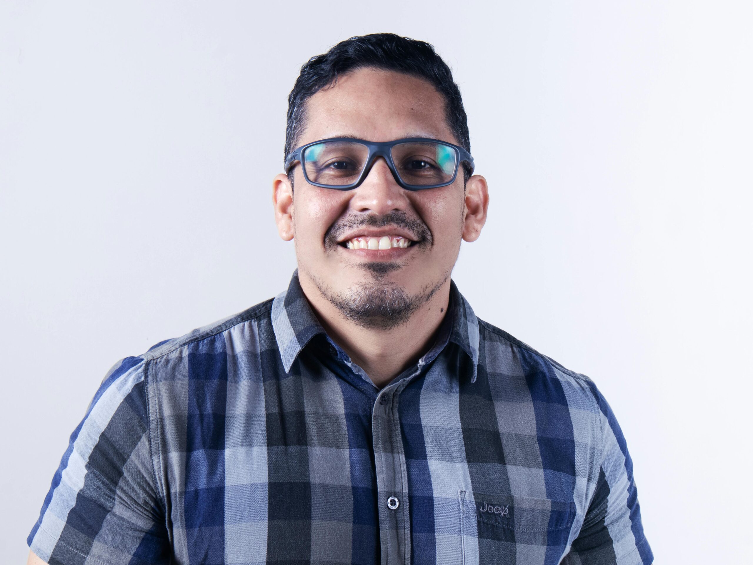 Casual portrait of a smiling man wearing glasses and a plaid shirt.