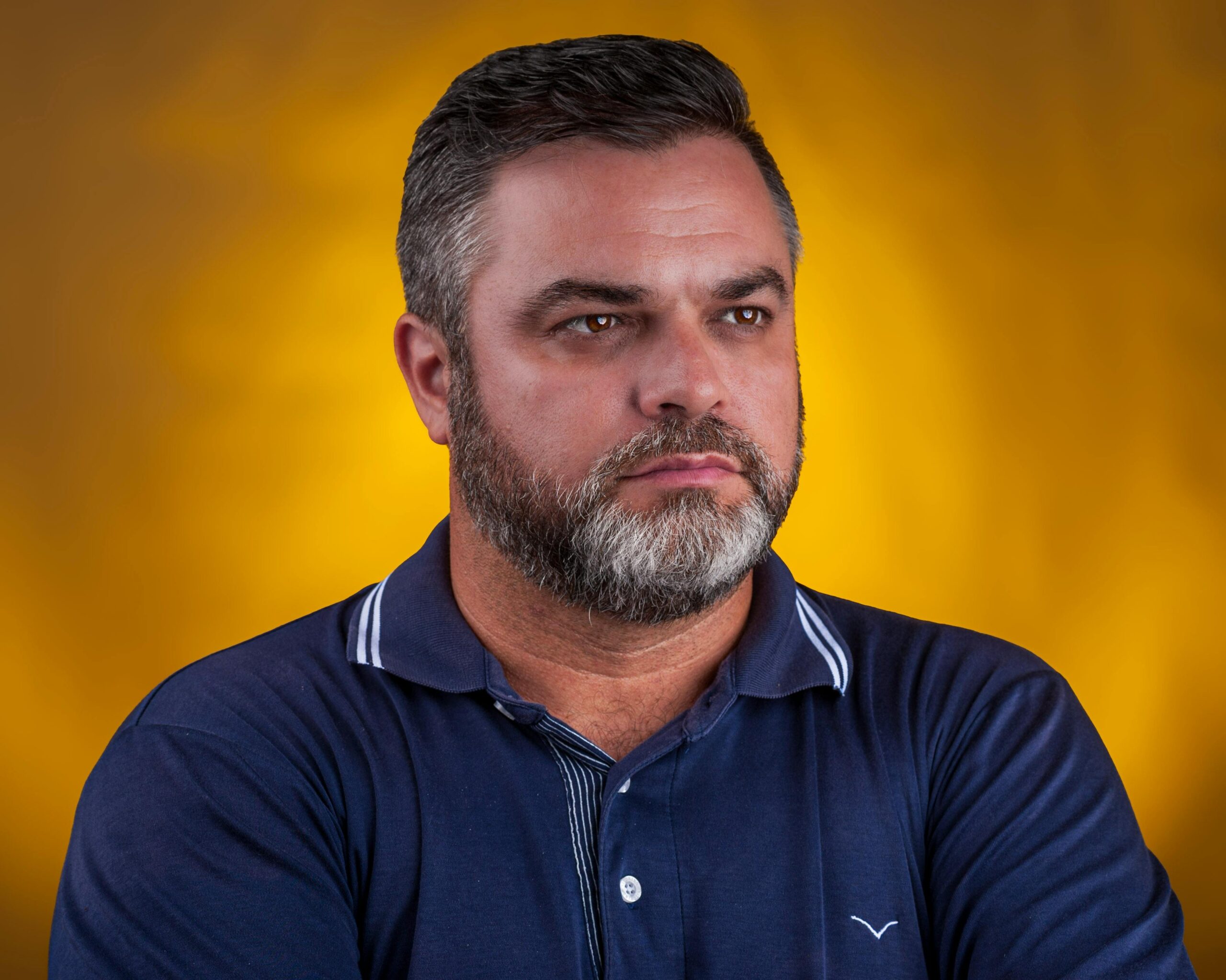 A mature man with a beard looks thoughtfully, set against a striking yellow background.